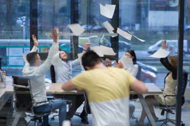 Bir grup genç iş adamı iş yerlerindeki başarılarını kutlarken dokümanları fırlatıyor ve mutlu görünüyorlar.