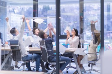 Bir grup genç iş adamı iş yerlerindeki başarılarını kutlarken dokümanları fırlatıyor ve mutlu görünüyorlar.