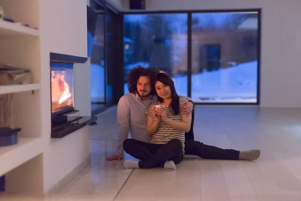 Feliz casal multiétnico sentado na frente da lareira — Fotografia de Stock