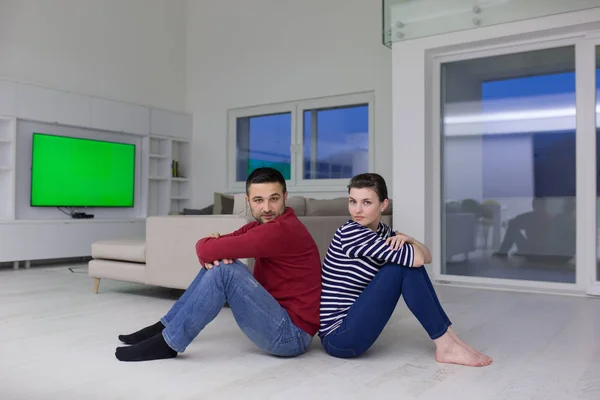 Молода пара сидить спиною один до одного на підлозі — стокове фото