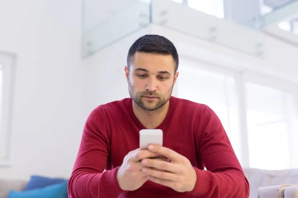 Jonge man met behulp van een mobiele telefoon thuis — Stockfoto