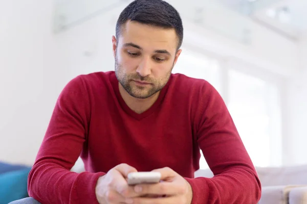 Jonge man met behulp van een mobiele telefoon thuis — Stockfoto