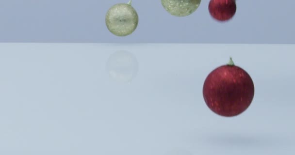 boules de Noël rouges et dorées et décoration tombent et rebondissent au ralenti sur fond blanc réfléchissant  