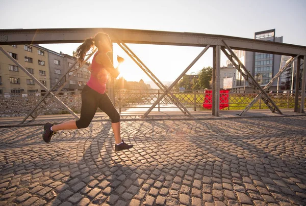 Kvinna som jogging över bron på solig morgon — Stockfoto