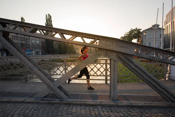 Kvinna som jogging över bron på solig morgon — Stockfoto