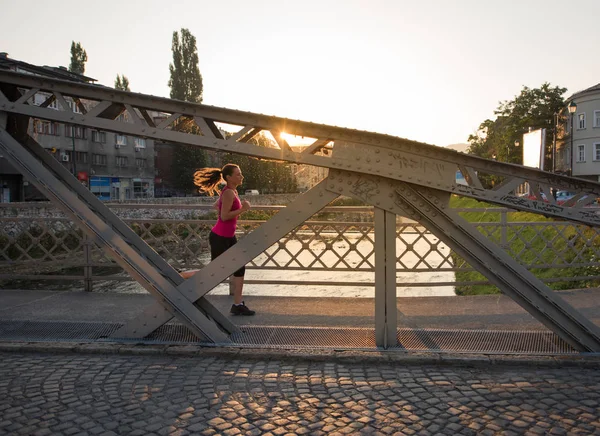Kvinna som jogging över bron på solig morgon — Stockfoto