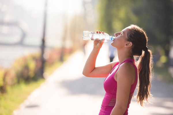 woman drinking water from a bottle after jogging