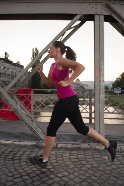 Femme jogging à travers le pont au matin ensoleillé — Photo