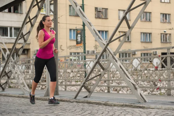 Kvinna som jogging över bron på solig morgon — Stockfoto