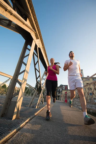 Giovani coppie che fanno jogging attraverso il ponte in città — Foto Stock