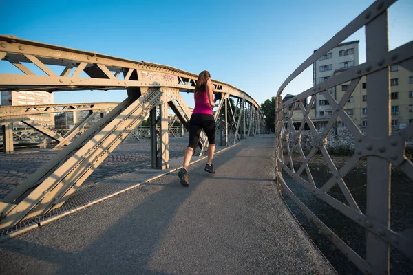 Kvinna som jogging över bron på solig morgon — Stockfoto