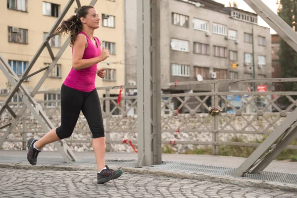 Kvinna som jogging över bron på solig morgon — Stockfoto