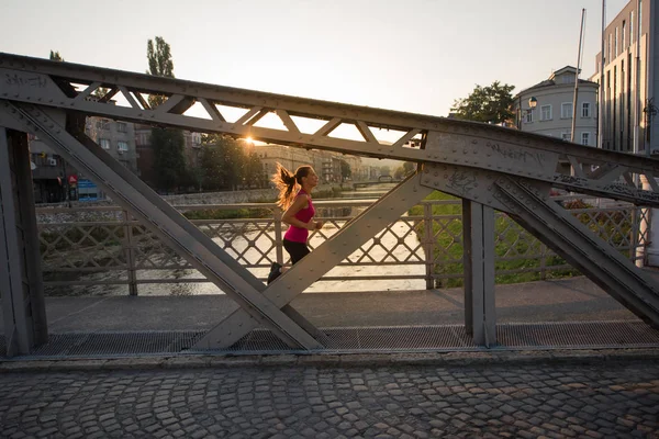 Kvinna som jogging över bron på solig morgon — Stockfoto