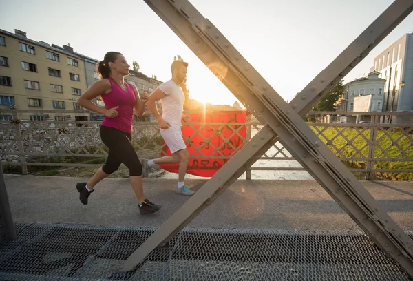 Ungt par jogging över bron i staden — Stockfoto