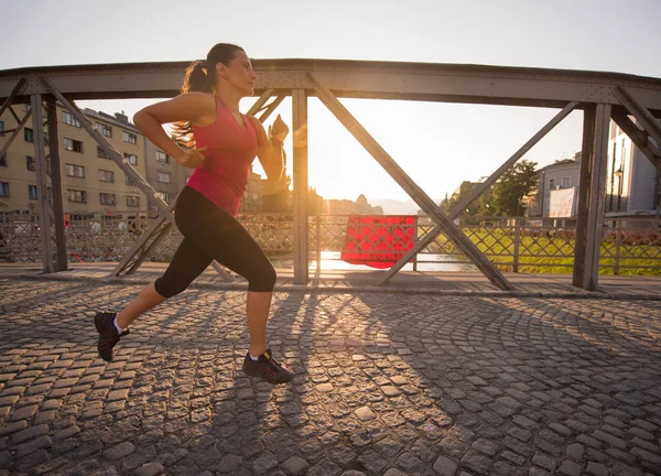 Kobieta, jogging przez most w słoneczny poranek — Zdjęcie stockowe