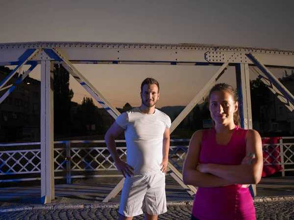 Portrait of couple jogging across the bridge in the city — Stock Photo, Image