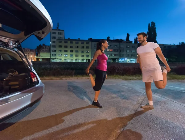 ジョギング カップル ウォーミング アップや夜の街で実行する前にストレッチ — ストック写真