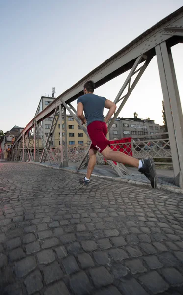 Młody Człowiek Sportowy Jogging Przez Most Słoneczny Poranek Mieście — Zdjęcie stockowe