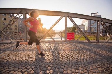 Sportif kadın köprüden güneşli sabah şehirde koşu.