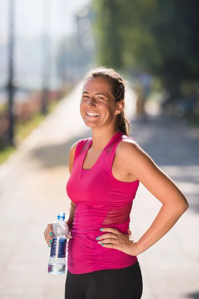 アスリート女性は晴れた日に市内でジョギングした後ボトルから水を飲む — ストック写真