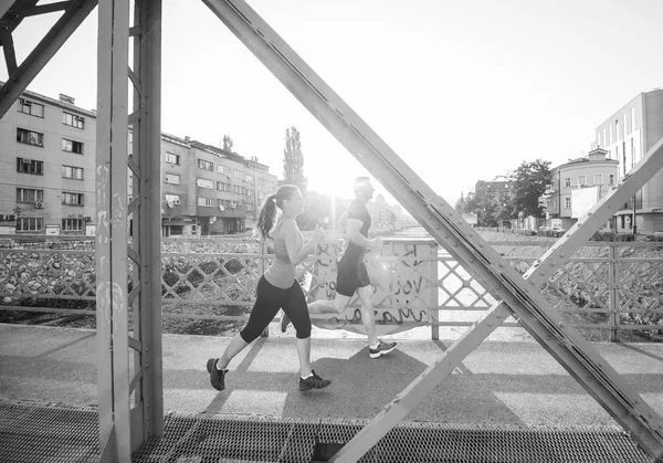 都市スポーツ 晴れた朝に市内の橋を渡ってジョギング健康な若いカップル — ストック写真