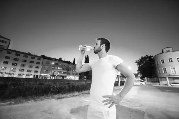 青年体育男子饮水后 在城市的夜间运行会议 — 图库照片