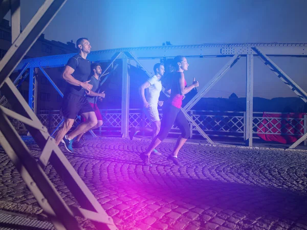 都市スポーツ 市内の橋を渡って夜に早朝ジョギング健康な若者のグループ — ストック写真