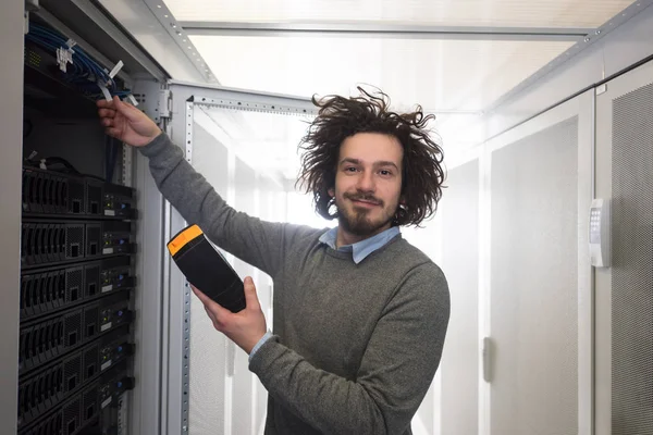 young IT technician using digital cable analyzer on server in large data center