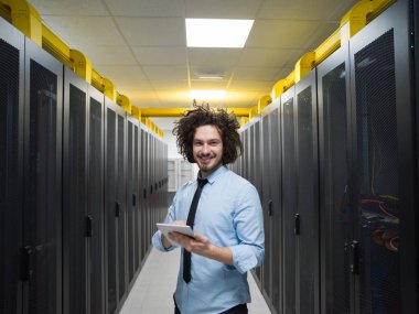 Modern veri merkezindeki sunucu odasında bir tablet bilgisayar üzerinde çalışan erkek bilişim mühendisi