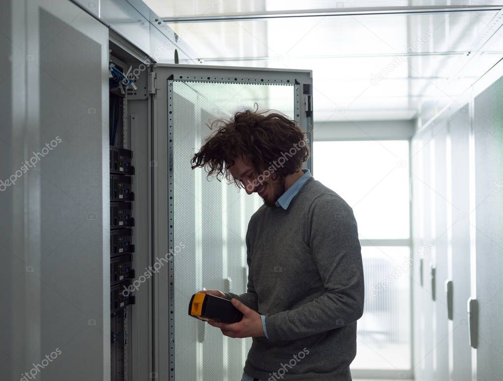 young IT technician using digital cable analyzer on server in large data center