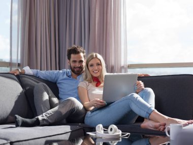 Genç çift, lüks ev koltuk kanepe oturma odasında dizüstü bilgisayar okuma kullanarak rahatlatıcı.