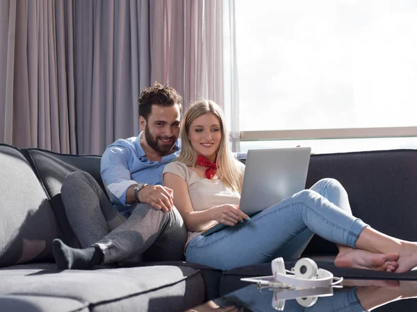 年轻夫妇放松在豪华家庭使用笔记本电脑阅读在客厅的沙发沙发 — 图库照片