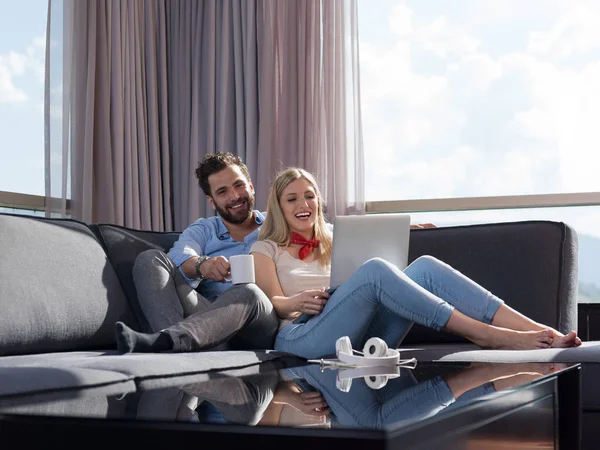 若いカップルの贅沢なソファー ソファのリビング ルームでラップトップ コンピューターの読み取りを使用して家でリラックス ロイヤリティフリーのストック画像
