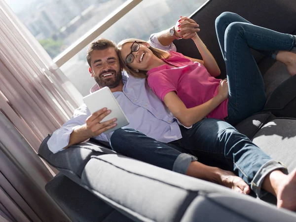 在客厅沙发上 一对年轻夫妇用平板电脑在客厅里看书来放松自己 — 图库照片
