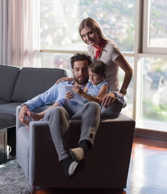 Mutlu Genç Aile, kanepede oturup tabletle birlikte oynuyor.