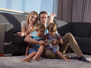 Mutlu Genç Aile, kanepede oturup tabletle birlikte oynuyor.