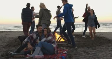 Gün batımında kumsalda şenlik ateşi etrafında dans eden bir grup arkadaş.