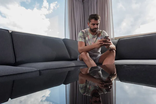 Jovem homem casual usando um telefone celular em casa — Fotografia de Stock