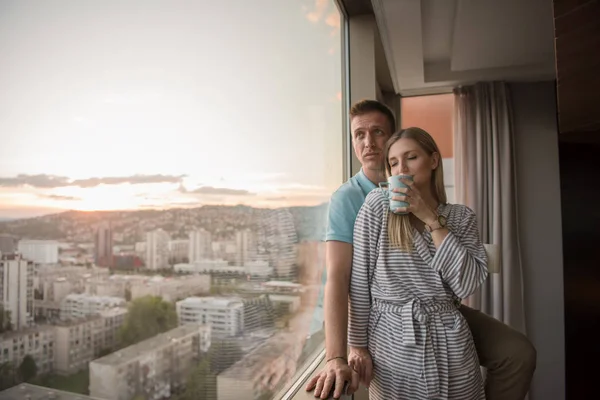 夜コーヒーや窓のそばに立っている間都市の美しい日没の風景を楽しんでロマンチックな幸せな若いカップル — ストック写真