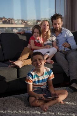Mutlu çift çocuklarla evde kanepede tablet bilgisayar kullanarak vakit geçiriyor.