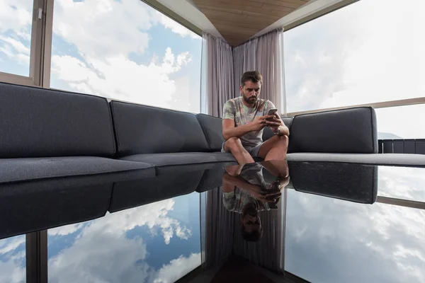 Joven hombre casual usando un teléfono móvil en casa — Foto de Stock