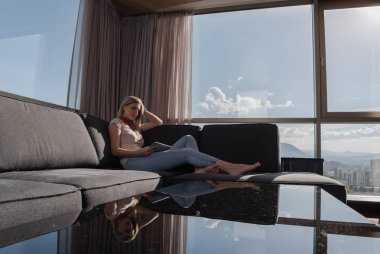 güzel genç bir kadın kanepede oturup tablet bilgisayar kullanarak internette sörf yapıyor.