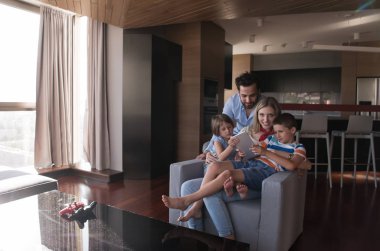 Mutlu çift çocuklarla vakit geçiriyor. Evdeki koltukta tablet bilgisayar kullanıyorlar.