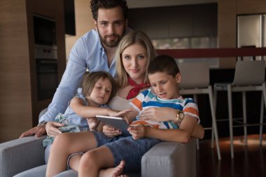 Mutlu çift çocuklarla vakit geçiriyor. Evdeki koltukta tablet bilgisayar kullanıyorlar.