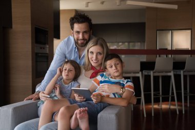 Mutlu çift çocuklarla vakit geçiriyor. Evdeki koltukta tablet bilgisayar kullanıyorlar.