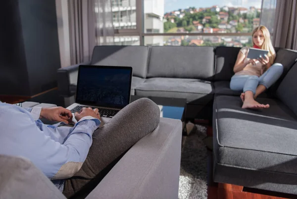 Genç Çift Kanepede Pencerenin Yanında Tablet Dizüstü Bilgisayar Kullanarak Rahatlıyor — Stok fotoğraf