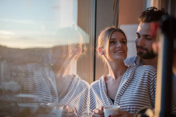 浪漫愉快的年轻夫妇享受傍晚咖啡和美丽的夕阳景观的城市 而站在窗口 — 图库照片