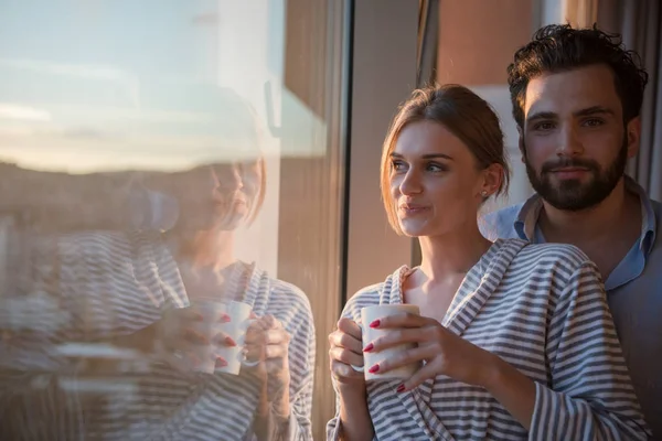 浪漫愉快的年轻夫妇享受傍晚咖啡和美丽的夕阳景观的城市 而站在窗口 — 图库照片