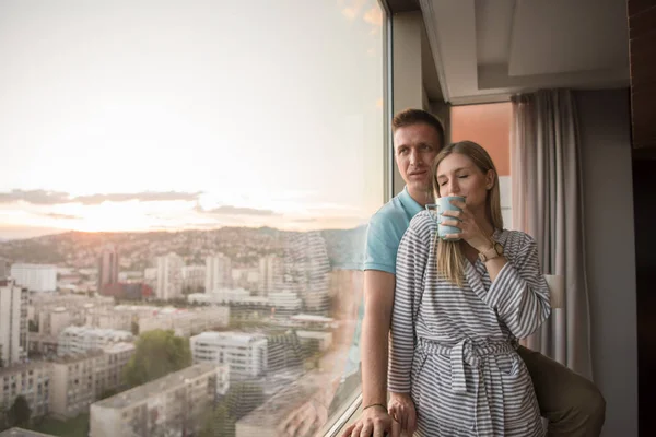 夜コーヒーや窓のそばに立っている間都市の美しい日没の風景を楽しんでロマンチックな幸せな若いカップル — ストック写真