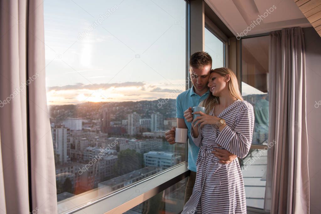 romantic happy young couple enjoying evening coffee and beautiful sunset landscape of the city while standing by the window